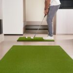 Man practicing putting on an artificial turf mat indoors for golf training.