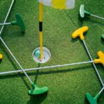 Top view of colorful mini golf putters around a hole on artificial grass.
