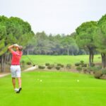 Back view of a golfer swinging a club on a lush golf course in Antalya, Türkiye.