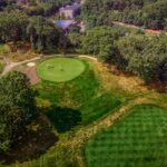 Aerial view of a lush golf course surrounded by trees, showcasing the vibrant greens under a sunny sky.