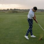 A man swings a golf club on a lush green course during sunset, capturing the essence of a serene golfing experience.