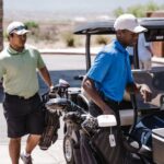 Two men prepare their golf equipment on a sunny day using a golf cart.