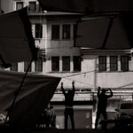 Black and white photo of silhouetted figures adjusting awnings in an urban setting.