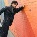 Athletic man in sports attire stretching against a vibrant mural wall outdoors.