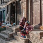 Two elderly women sit outside their home in Bhaktapur, Nepal, enjoying sunlight.