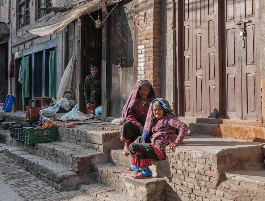 Two elderly women sit outside their home in Bhaktapur, Nepal, enjoying sunlight.