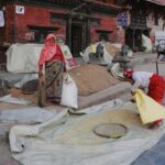 Women working with grain outside a traditional building in an urban area, showcasing local culture.
