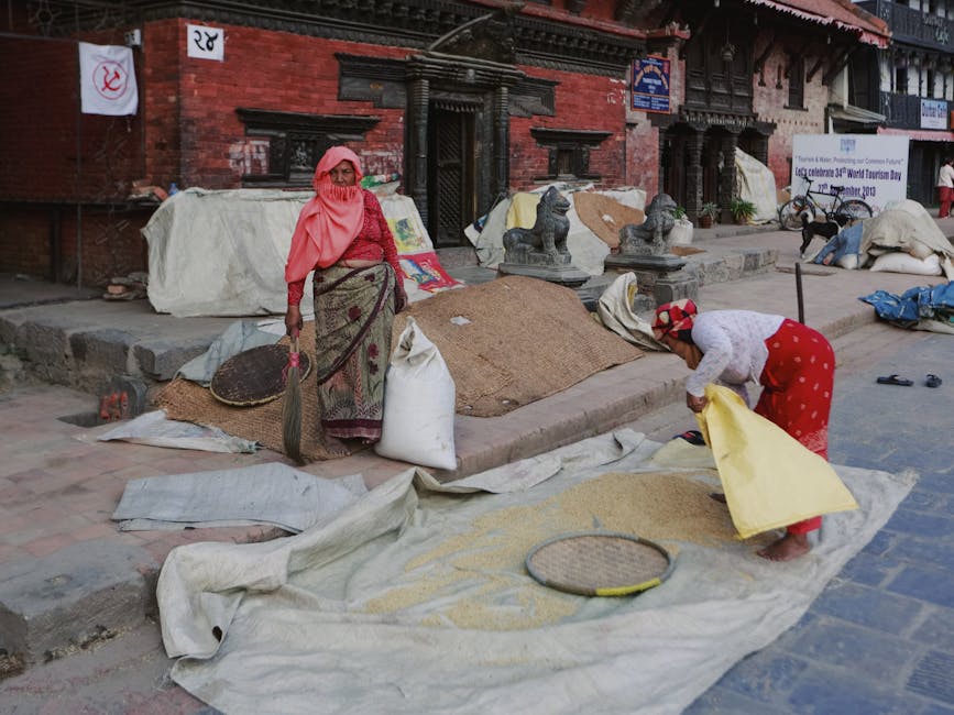 Women working with grain outside a traditional building in an urban area, showcasing local culture.