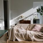 Sunlit cozy apartment interior featuring a comfortable beige-covered sofa, potted plants, and warm decor.