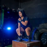 Focused woman squatting with kettlebell in gym setting, showcasing strength and determination.