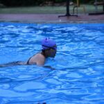 An adult woman swimmer practicing strokes in an outdoor pool with a blue swim cap.
