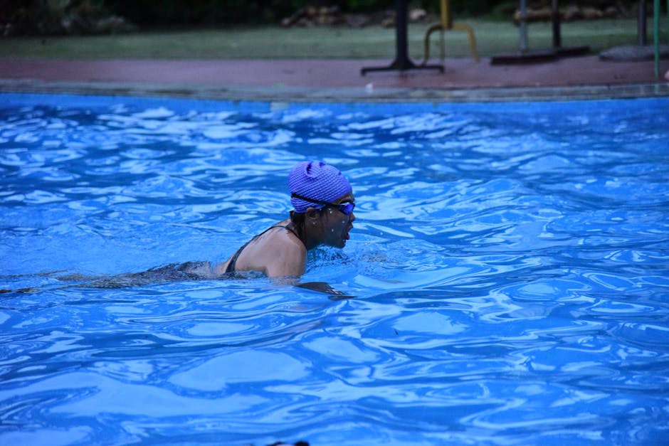 An adult woman swimmer practicing strokes in an outdoor pool with a blue swim cap.