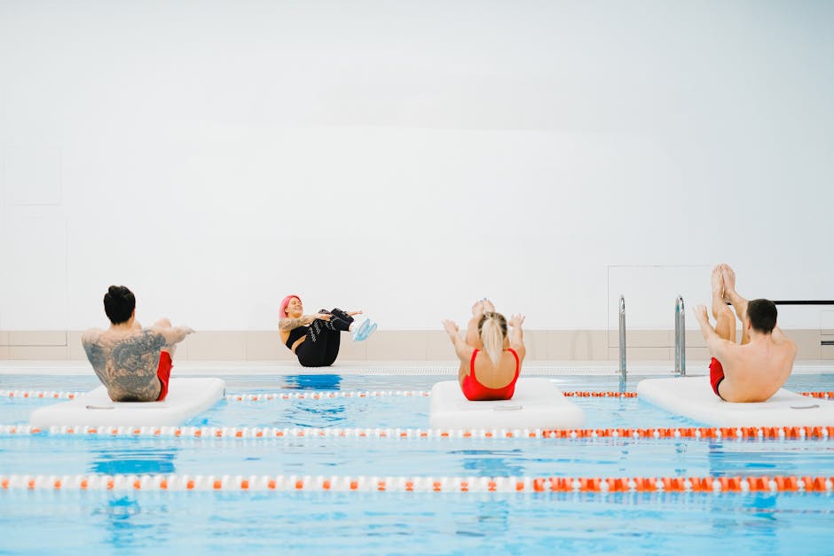 Group exercising on floating mats in an indoor swimming pool setting with a trainer.