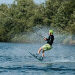 A man wakeboarding on a beautiful sunny day, creating splashes while gliding across a lake.