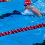 Swimmer in competitive race at indoor swimming pool with clear blue water.