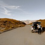Person organizing gear in SUV on isolated desert road, perfect for travel enthusiasts.