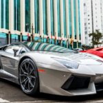 Luxury silver sports car parked in front of modern glass facade building.