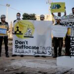 Protest in Idlib, Syria against chemical attacks, featuring banners and activists in protective gear.