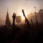 A vibrant traditional festival in Karbala during sunset with silhouettes and raised hands.