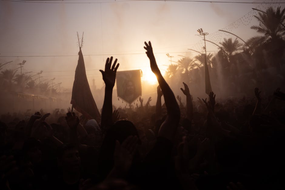 A vibrant traditional festival in Karbala during sunset with silhouettes and raised hands.